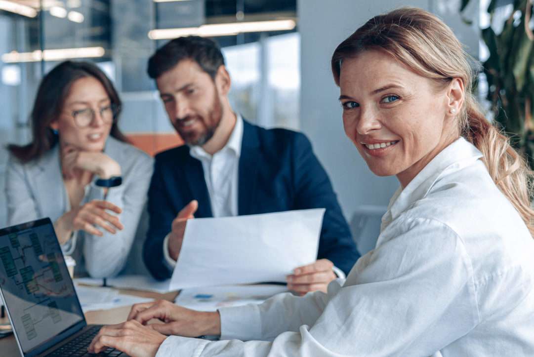 confident smiling businesswoman sitting at the office with group of colleagues, on background